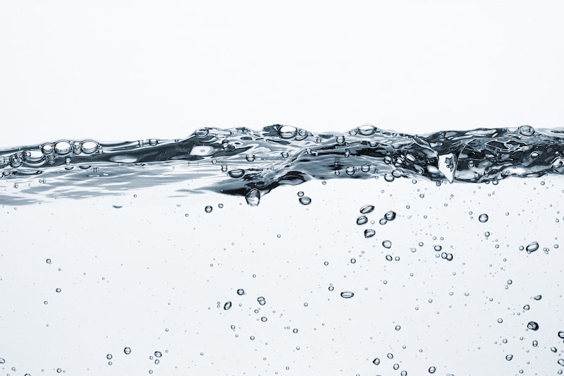 Close-up of clear water with bubbles and a light reflection on a white background