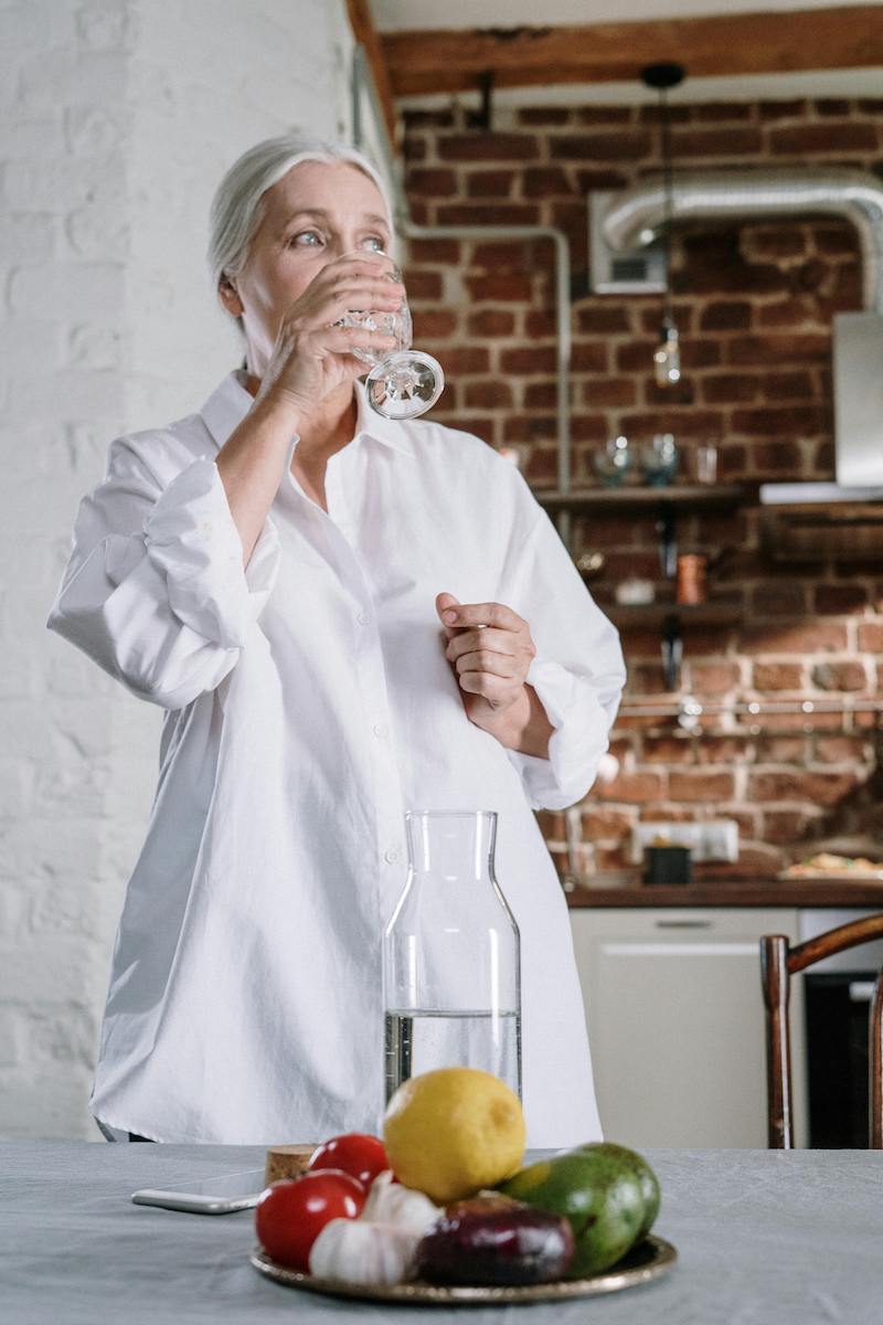 woman drinking ro water in a kitchen with fruits on the table