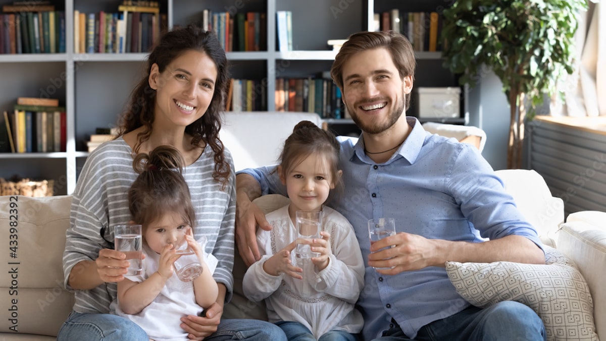 Family of four sitting on a couch holding glasses of ro water